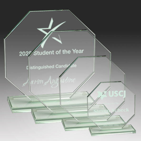 Clear glass awards with engraved text on a dark background