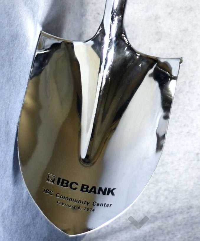 Metallic shovel with 'IBC Bank' branding on a textured gray background