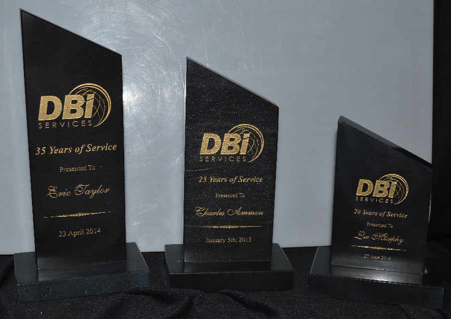 Three black and gold DBI Services award plaques on a gray surface.